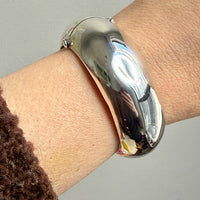 Silver bangle on a wrist against a neutral background