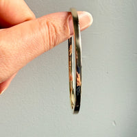 Hand holding a gold bangle against a plain background