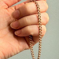 Rose gold chain held between fingers against a neutral background