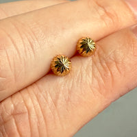 Gold earrings with star design held between two fingers against a neutral background