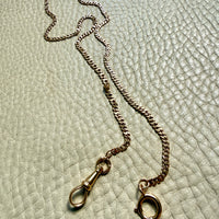 18k gold watch chain necklace with dog clip on a textured light gray background
