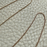 18k gold curb link necklace on a textured light gray surface