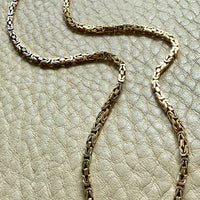 14k gold Gold byzantine chain necklace on a textured beige surface penelopepenelope.com fine jewelry