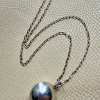 Silver necklace with a round pendant on a textured beige surface