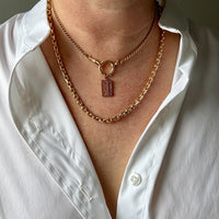 Person wearing a gold chain necklace with a pendant on a white shirt.
