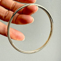gold bangle held by a hand against a gray background