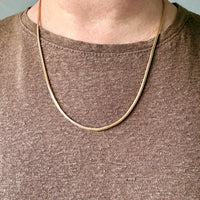 Gold chain necklace worn by a person on a plain background