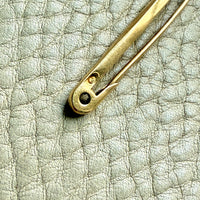 18k gold vintage safety pin brooch on a textured light gray background