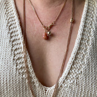 Necklaces with pendants on a person wearing a beige knit cardigan.