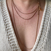 Close-up of a person wearing a delicate gold necklace with a textured beige sweater.