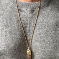 Necklace with an eye-shaped pendant and tassel worn by a person in a gray sweater.