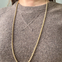 Gold chain necklace on a person wearing a brown sweater.