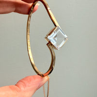 Gold bracelet with a clear crystal on a plain background. PenelopePenelope.com