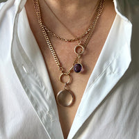 Gold chain necklace with a purple gemstone on a white shirt. PenelopePenelope.com
