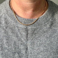Person wearing a gray sweater and gold necklace against a neutral background