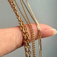 Three gold chains held by a hand against a neutral background