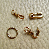 Four small gold jewelry findings arranged on a textured beige leather surface
