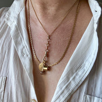 Close-up of a person wearing a gold necklace with a pendant, against a neutral background. Penelope Penelope Vintage Jewelry