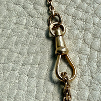 Close-up of a 18k gold chain with a swivel dog clip clasp on a textured light gray background