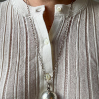 Close-up of a silver necklace with a large pendant on a white shirt.