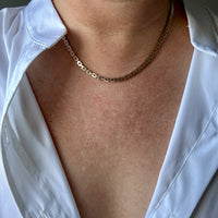 Gold chain necklace worn by a person in a white shirt.