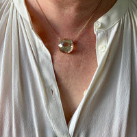 Necklace with a large pendant worn by a person in a white shirt.