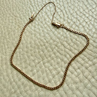 An 18k gold chain bracelet with a box clasp and safety chain, laid out on a textured off-white leather surface.