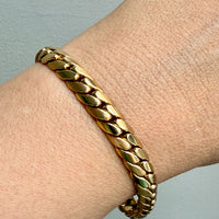Gold chain bracelet on a wrist against a light gray background