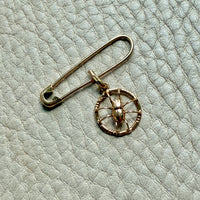 Gold safety pin with a circular spider pendant on a light gray textured background