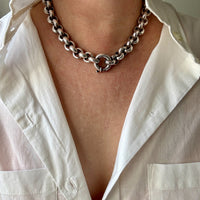 Person wearing a silver chain necklace with a white shirt.