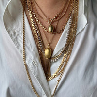 Person wearing multiple gold necklaces on a white shirt