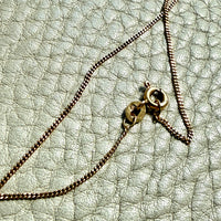 Close-up of a gold necklace on a textured light gray surface