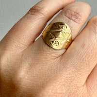 Gold ring with intricate design on a finger against a neutral background