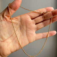 Gold chain held in a hand against a neutral background