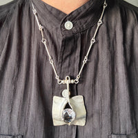 Person wearing a dark shirt with a necklace featuring a unique pendant.