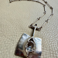 Silver necklace with a pendant on a textured beige surface