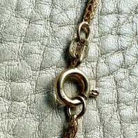 Close-up of a gold chain with a clasp on a textured silver surface
