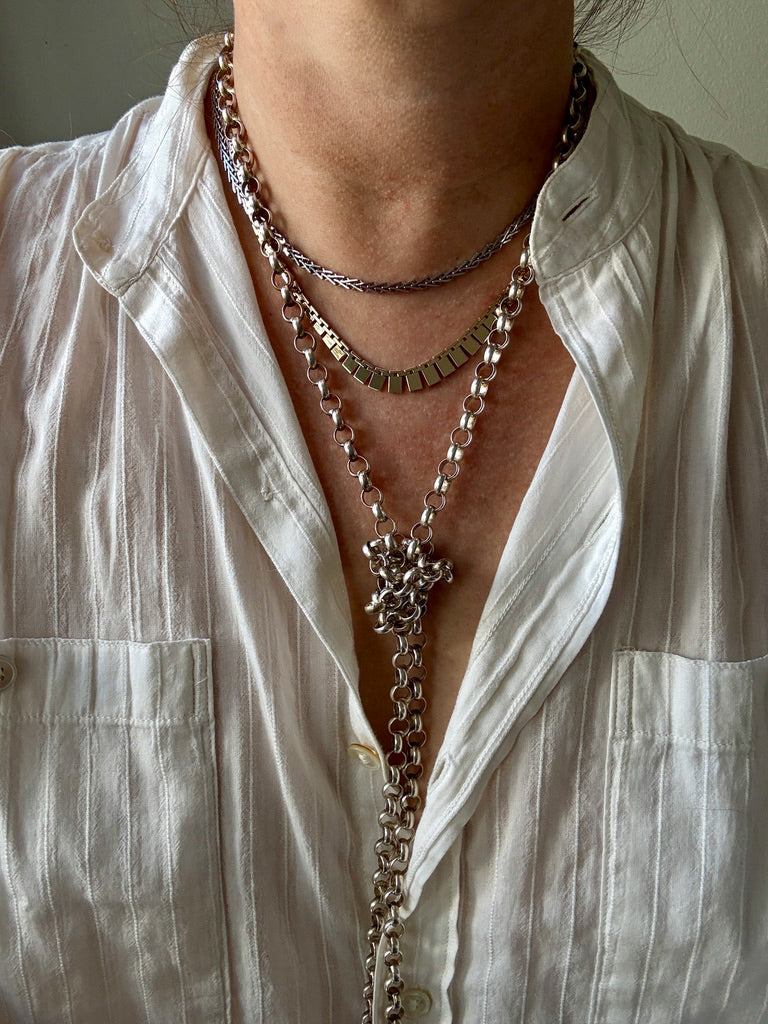 Close-up of a person wearing multiple necklaces with a white shirt.