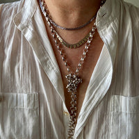 Close-up of a person wearing multiple necklaces with a white shirt.