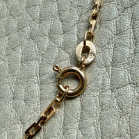 Close-up of a gold chain with a clasp on a textured light gray surface