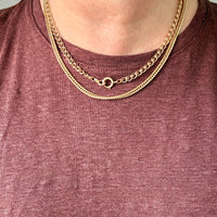 A close-up of a person's neck wearing two layered gold chain necklaces over a heathered mauve-brown t-shirt.