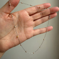 Hand holding a delicate beaded necklace against a neutral background