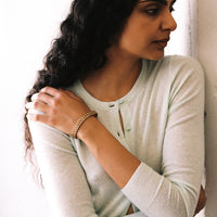 A person wearing a light green or beige long-sleeve top showcasing a gold honeycomb link triple row bracelet on their wrist.