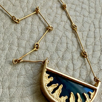 Gold necklace with a half-circle pendant on a textured beige background