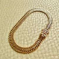 A vintage 18k gold herringbone chain braceley with a woven, braided link design, arranged in an oval shape on a textured beige leather background.