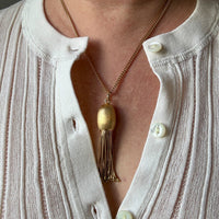 Gold necklace with a vintage 18k gold tassel pendant worn by a person in a white cardigan. penelopepenelope.com