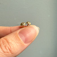 Gold earrings held between fingers against a neutral background