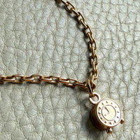 Gold chain necklace with a round pendant on a textured light gray background