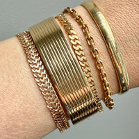 Gold bracelets on a wrist against a neutral background