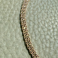 Gold chain detail showing repairs on a textured neutral surface